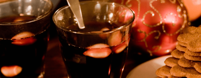 photo of two glasses of glögg with almonds and next to them a plate of gingerbread cookies and a christmas ornament