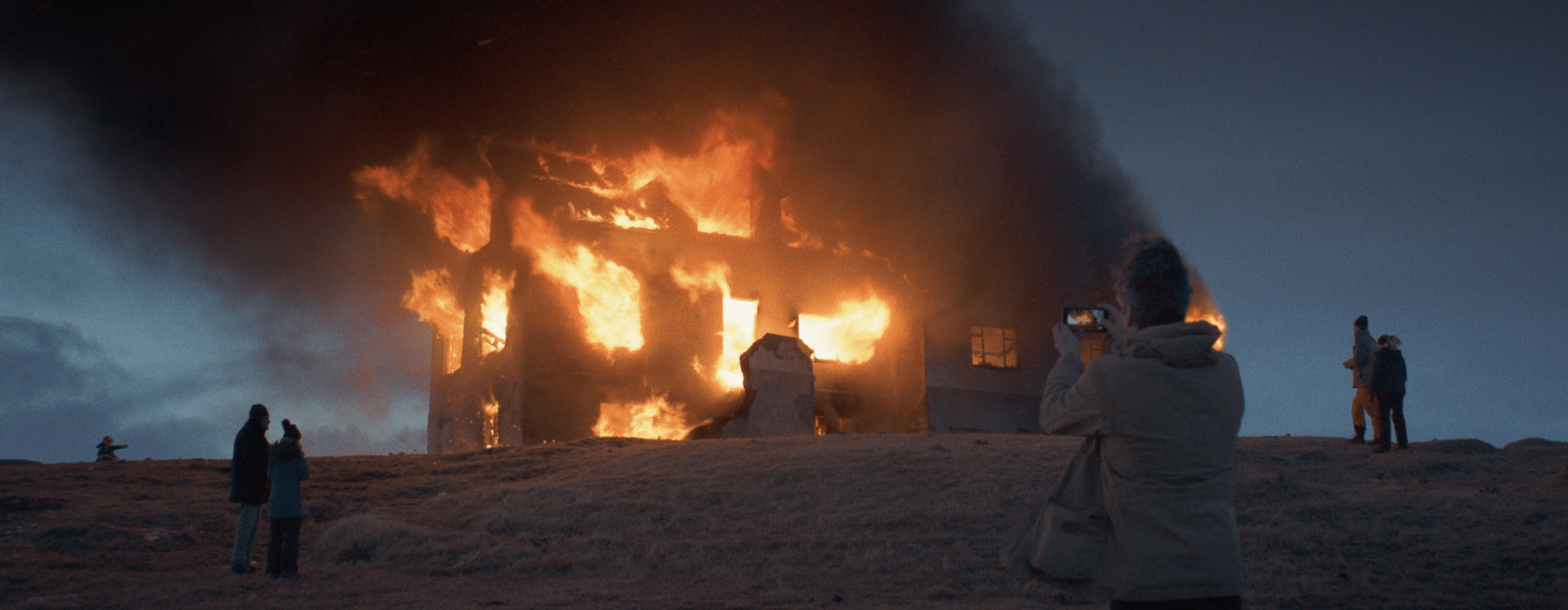 a photo of a burning building, in the foreground a person taking a picture of the building with their cellphone
